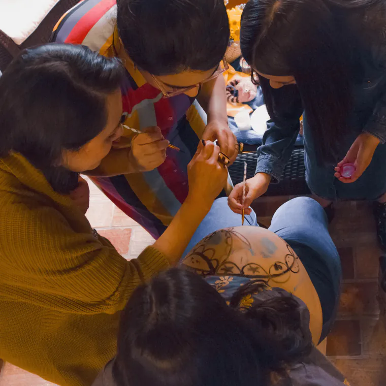 Varias mujeres pintando el vientre de una embarazada durante una ceremonia