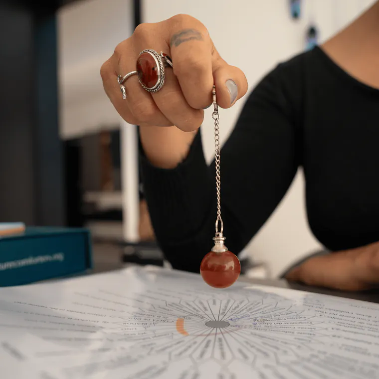 Mano sosteniendo un péndulo de piedra roja sobre un gráfico de Terapia de Respuesta Espiritual