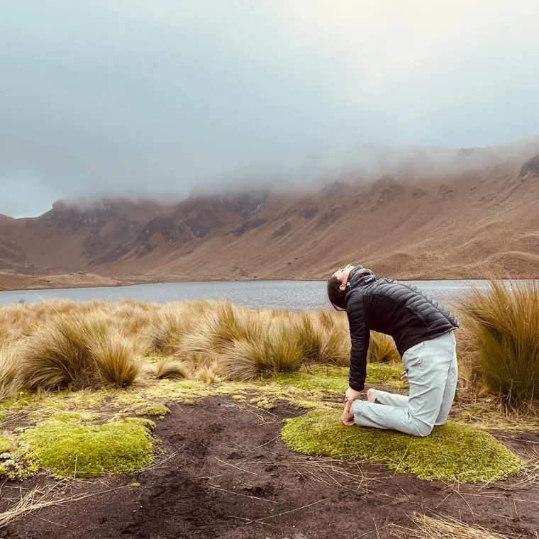Mujer en postura de yoga arrodillada frente a una laguna de páramo