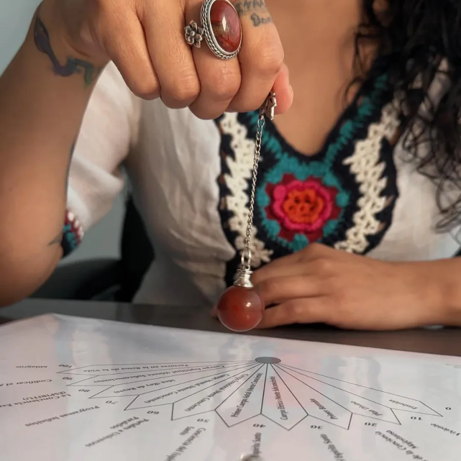 Gabriela Ormaza sosteniendo un péndulo de jaspe rojo sobre un gráfico