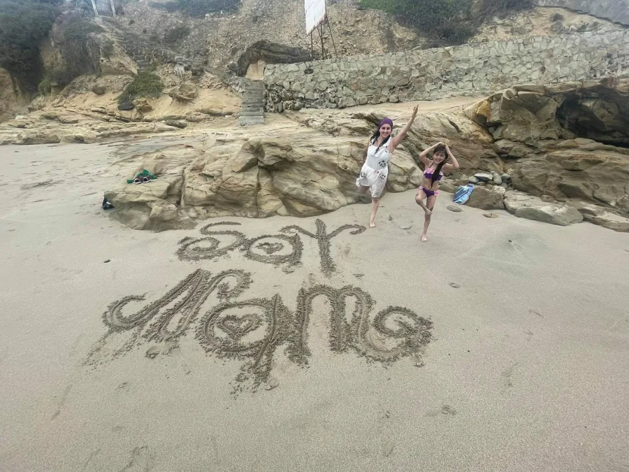 Gabriela junto a su hija en la playa, sobre la arena escrito "Soy Mamá"